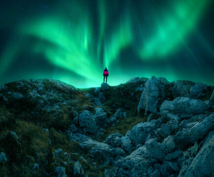 northern lights and young woman on mountain peak at night. aurora borealis, stones and silhouette of