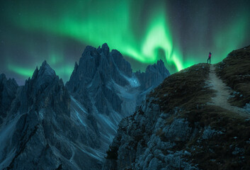 Wall Mural - northern lights and young woman on mountain peak at night. aurora borealis and silhouette of alone g