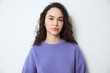 © Folenial - Portrait of a serious confident young jewish woman with long brown curly hair and clean face wearing a purple sweater and looking directly at the camera over a gray background in studio shot.