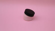 Envase de plástico para crema facial en color rosa con tapadera negra medio abierta. 