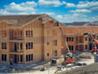 Hard working team constructing multi-family housing apartments: Construction workers utilizing heavy duty equipment, trucks, and telescopic boom lifts to finish exterior walls and roof with plywood