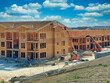 Hard working team constructing multi-family housing apartments: Construction workers utilizing heavy duty equipment, trucks, and articulating boom lifts to finish exterior walls and roof with plywood