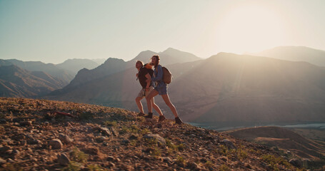 Hipster young couple with backpack enjoying sunset on peak of foggy mountain. Young caucasian couple backpacking together, exploring beautiful mountains - adventure, freedom concept