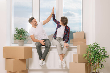 Canvas Print - Happy couple giving high five while sitting on windowsill in new apartment. Moving day