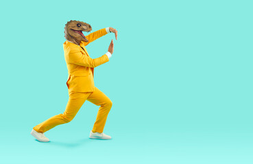 Wall Mural - Cheerful and eccentric man in rubber dinosaur mask shows funny dance moves near copy space. Man in yellow bright suit and absurd animal mask on his head isolated on turquoise background. Full length.