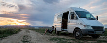 Panoramic View Of Man Resting On Camping Chair Against Mini Van On Field During Sunset At Joshua Tree National Park