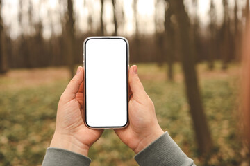 Hand holding phone with blank screen taking photo or selfie in the forest. There is no signal. The concept may relate to digital detox or business message