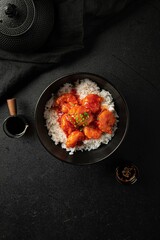 Poster - Portion of asian sweet and sour shrimp with rice on black background