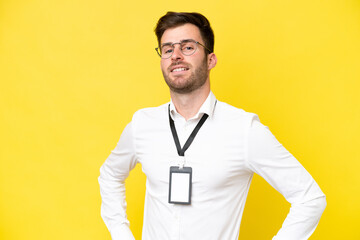 Wall Mural - Young caucasian with ID card isolated on yellow background posing with arms at hip and smiling