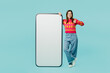 © ViDi Studio - Full body young woman wear bright casual clothes stand near big huge blank screen mobile cell phone smartphone with workspace mockup area show thumb up isolated on plain pastel blue cyan background.