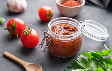 Wall Mural - Homemade tomato sauce for pizza or pasta in a jar on a dark background with fresh vegetables, herbs and spicy close up.