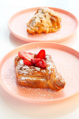 Strawberry danish pastry placed on a pink plate with almond croissant in the background.