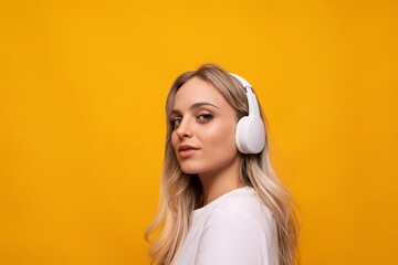 caucasian blonde woman posing in white headphones on orange background with empty space