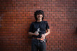 © Westend61 - Happy young man standing with camera in front of brick wall