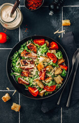 Wall Mural - Homemade Caesar salad with crispy chicken and tomatoes on a black tiled background