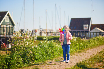 Wall Mural - Adorable preschooler girl with colorful pinwheel walking in picturesque village of Marken, North Holland, the Netherlands