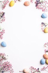 Wall Mural - Overhead shot of Easter composition with spring flowers and colorful quail eggs over white background. Springtime and Easter holiday concept with copy space. Top view