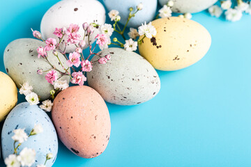 Wall Mural - Easter composition with spring flowers and colorful quail eggs over blue background. Springtime and Easter holiday concept with copy space.