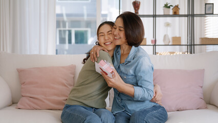 Wall Mural - May Mother's day young adult grown up child cuddle hug give flower gift box red heart card to mature middle aged mum. Love kiss care mom asia people sitting at home sofa happy smile enjoy family time.