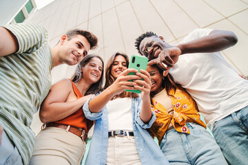 low angle view of multiracial group of young friends enjoying and smiling using their mobile phone a