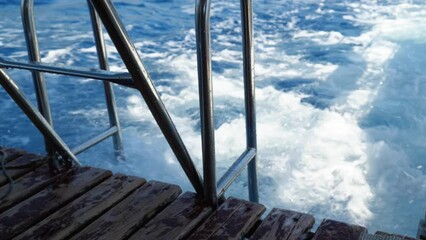 Wall Mural - A view of the stern of the ship with steel handrails and a bridge floating on the sea. The ship leaves behind shiny white foamy waves. The boat is bobbing on the waves. Close up. Slow motion