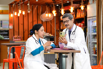 Poster - Indian male doctor showing some detail in smartphone and discussing with assistance doctor.