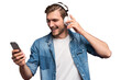 © opolja - Excited young man wearing jeans shirt standing isolated over transparent background, listening to music with earphones and mobile phone