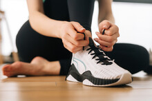 Close Up Hands Of Athletic Female Tying Shoelaces On Sports Shoe Preparing To Workout. Close-up Cropped Shot Of Unrecognizable Sporty Woman Tying Shoe Laces On Floor Preparing For Workout In Gym.