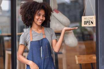 Wall Mural - Small business african woman is a waitress in an apron, the owner of the cafe stands at the door with a sign Open waiting for customers. Small business concept, cafes and restaurants