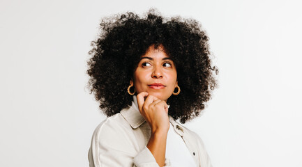 Wall Mural - Thoughtful woman with curly hair standing against a studio background