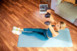 © gzorgz - Sporty woman using dumbbells and laptop while exercising at home