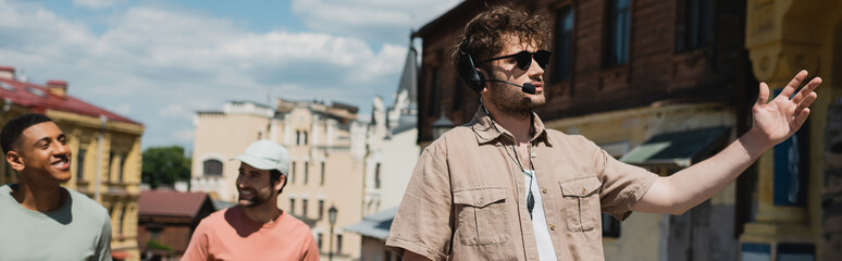 tour guide in sunglasses and headset pointing with hand during excursion on andrews descent in kyiv,