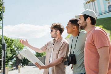 Wall Mural - side view of young guide with city map pointing with hand near multicultural travelers on andrews de