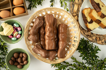 Wall Mural - Chocolate Easter bunnies in traditional Paschal wicker basket. Flat lay composition with eggs, candies, boxwood branches and loaf cake.