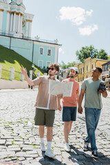 Wall Mural - full length of multiethnic tourists walking with tour guide holding travel map and pointing with han