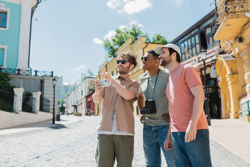 Wall Mural - smiling guide with mobile phone pointing with finger while leading tour for interracial men on podil