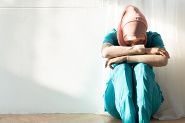 Unhappy - tired Muslim female surgeon doctor sitting on the floor in the hospital. Overworking problem and stress in medical staff concept.