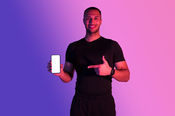 Wall Mural - Athletic African Guy Showing Smartphone Screen Over Purple Neon Background