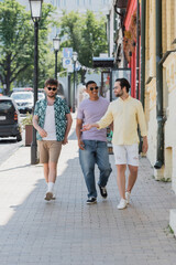 Wall Mural - smiling interracial friends in sunglasses walking on andrews descent in kyiv.