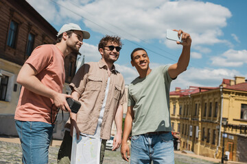 Wall Mural - cheerful african american traveler taking photo on smartphone with multiethnic men on andrews descen