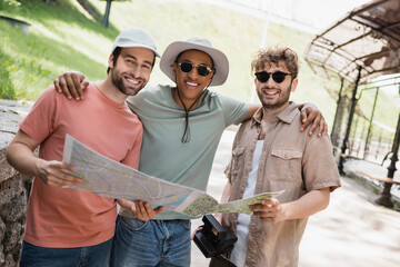 Wall Mural - carefree african american man in sun hat and sunglasses embracing friends on urban street.