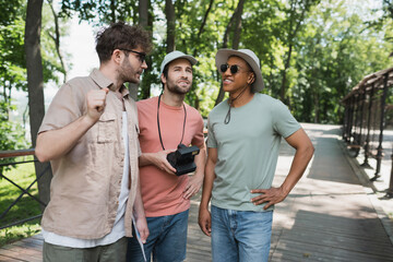 Wall Mural - bearded tourist with vintage camera looking away near multiethnic men during excursion in summer par