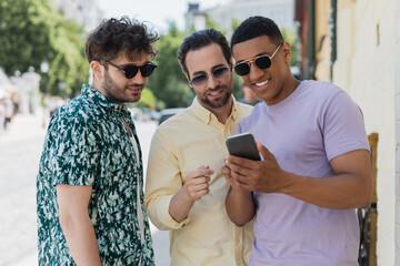 Wall Mural - multiethnic friends using mobile phone on urban street in summer.