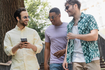 Wall Mural - positive multiethnic friends using smartphone while walking on stairs in park in summer.