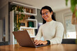 © bnenin - A smiling Asian businesswoman typing on a laptop, sitting in the living room.