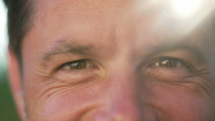 One happy man macro portrait face close up smiling outside with sunlight flare. 40s person with wrinkles closeup of eyes