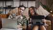 © saksit - Young couple using tablet and laptop together on sofa in living room at home