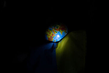 Wall Mural - A hand holds the flag of Ukraine and a globe in the dark