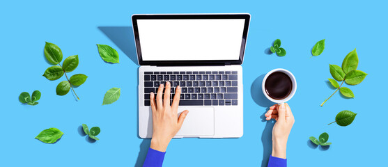 Wall Mural - Person using a laptop computer with green leaves - flat lay
