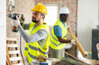 © JackF - Portrait of man builder working with handheld demolition hammer at indoor construction site, while his assistant carrying wooden materials
